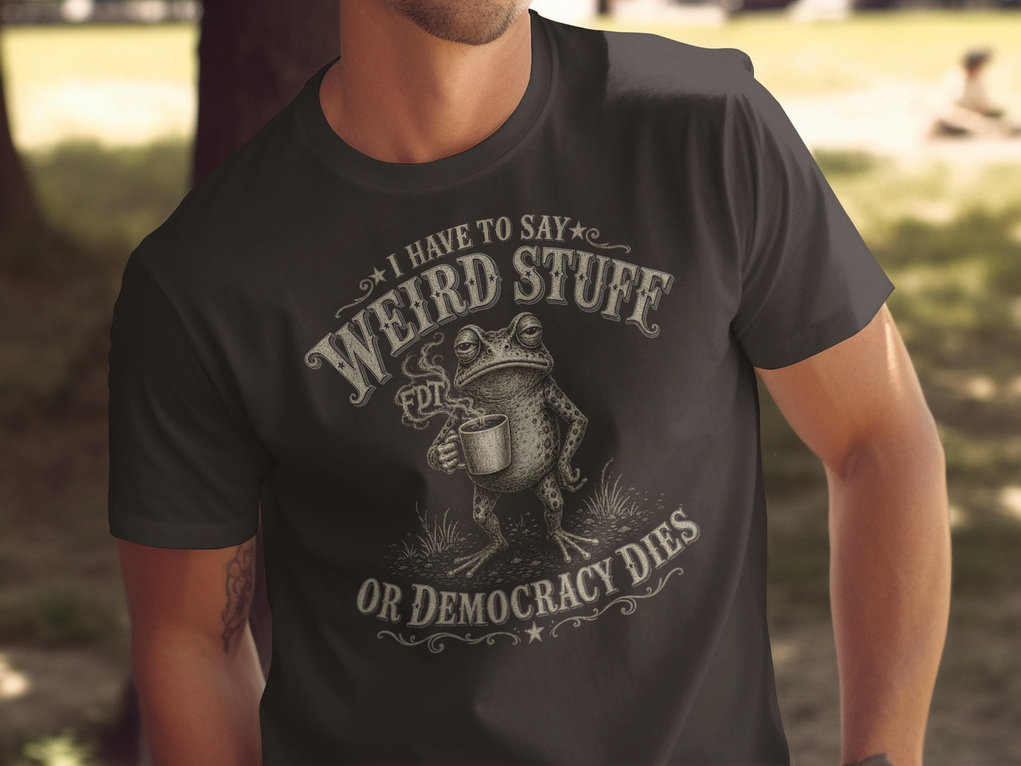 Dark t-shirt with "I have to say weird stuff or democracy dies" text and frog graphic.