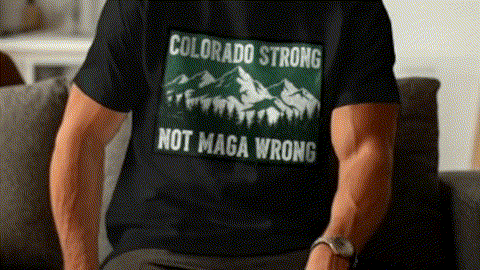 A person wearing a black t-shirt with a graphic design on it, which features a mountain range and the text "COLORADO STRONG NOT MAGA WRONG".