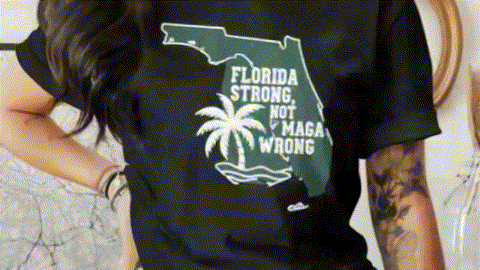 A person wearing a black t-shirt with a graphic design that says "Florida Strong Not MAGA Wrong" printed on it.