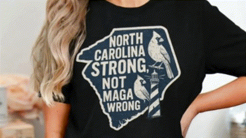 A woman wearing a black t-shirt with a graphic design that says "NORTH CAROLINA STRONG, NOT MAGA WRONG".