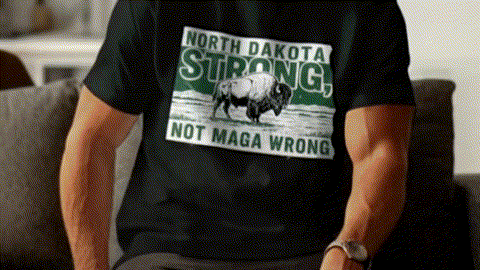 A person wearing a black t-shirt with a graphic design of a buffalo on it, along with the text "NORTH DAKOTA STRONG, NOT MAGA WRONG".