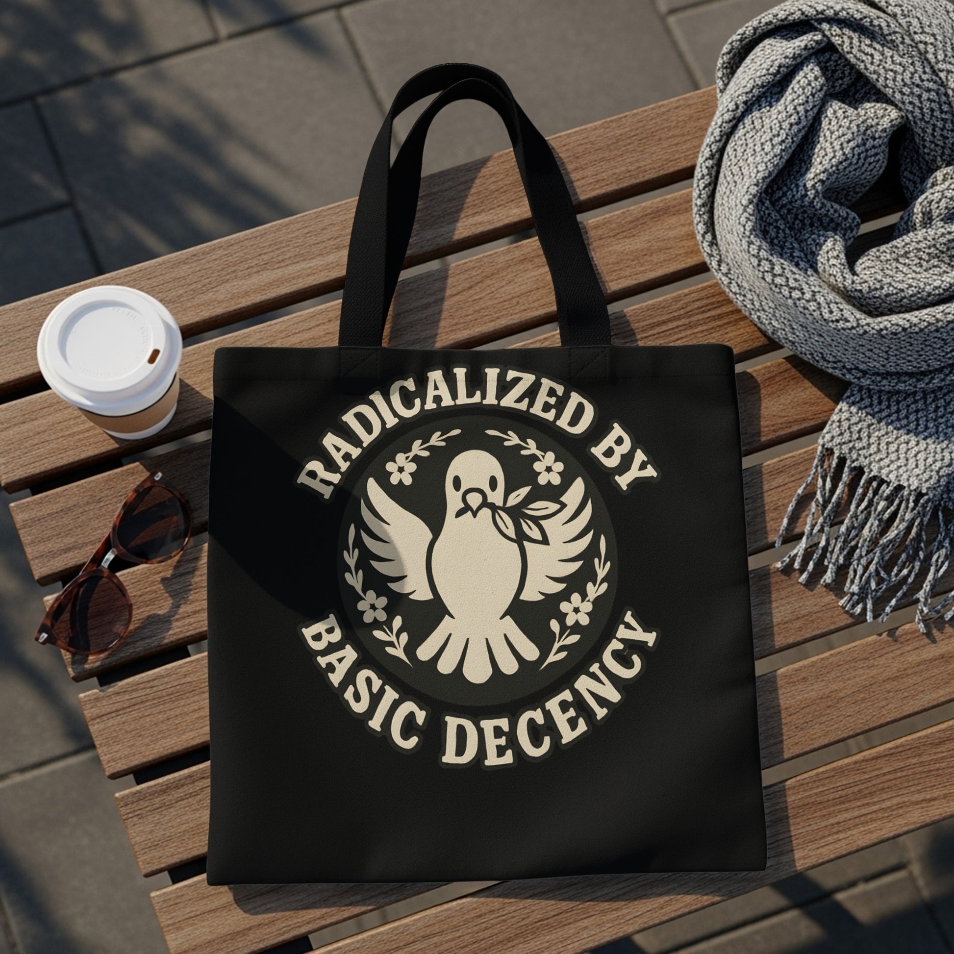 Black tote bag with "Radicalized by Basic Decency" text and a dove emblem.