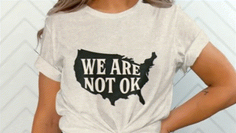A person wearing a white t-shirt with the text "WE ARE NOT OK" printed on it.