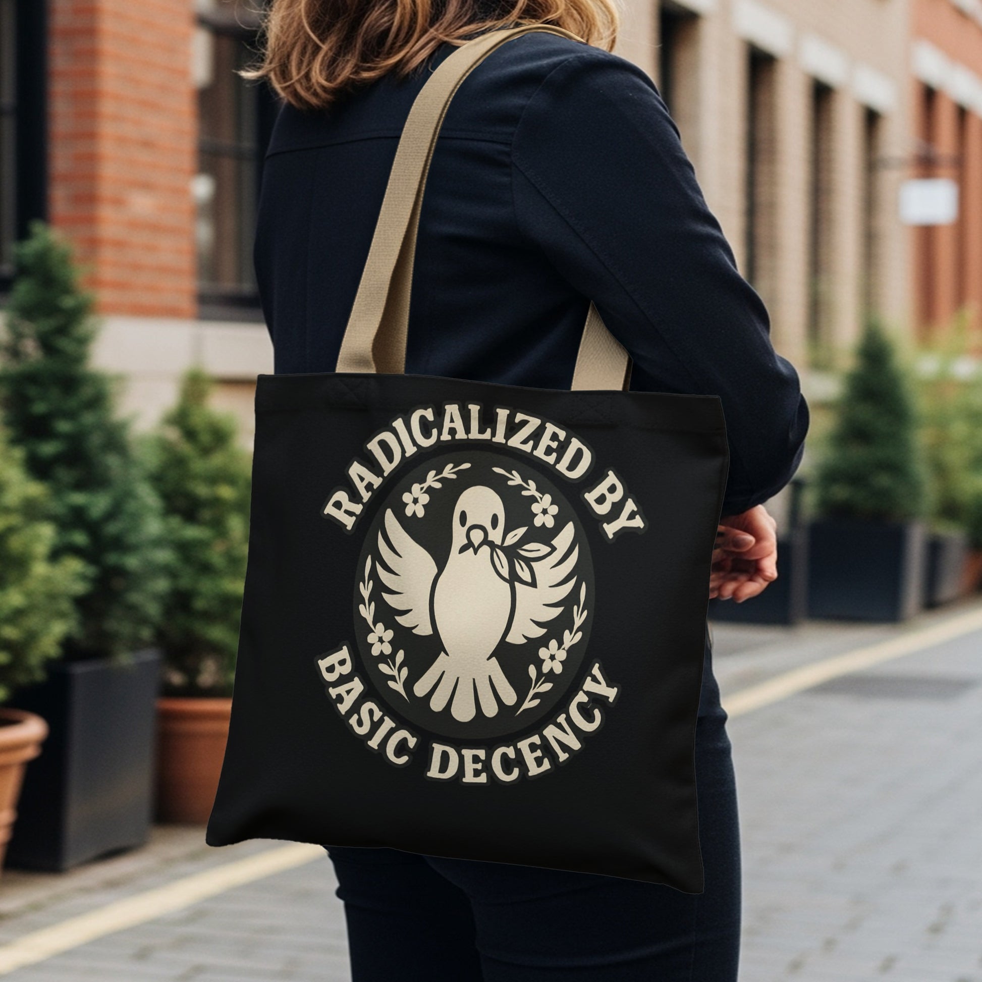 Black tote bag with "Radicalized by Basic Decency" and dove logo.