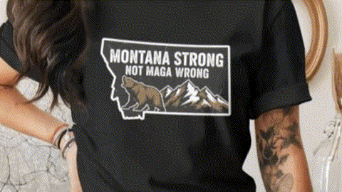 A person wearing a black t-shirt with a graphic design of a bear and mountains, along with the text "Montana Strong Not Maga Wrong".