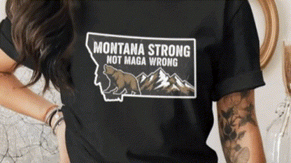 A person wearing a black t-shirt with a graphic design of a bear and mountains, along with the text "Montana Strong Not Maga Wrong".