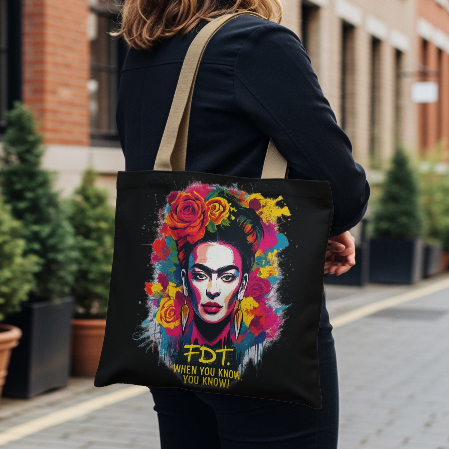 Frida Kahlo portrait on black tote bag with colorful flowers and yellow text.