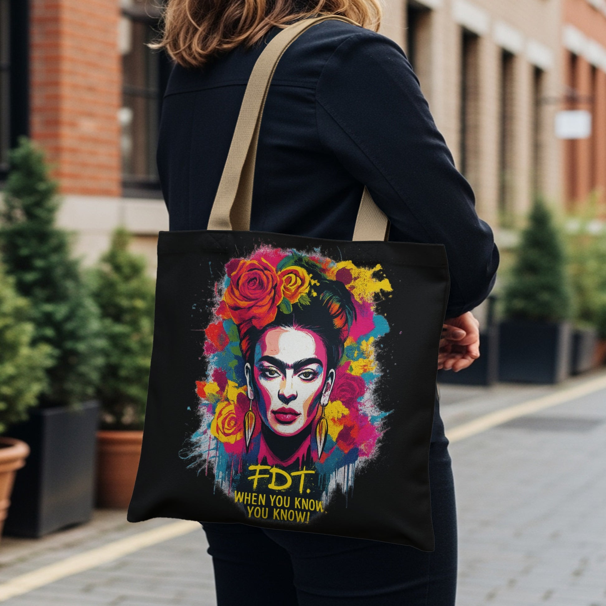 Frida Kahlo portrait on black tote bag with colorful flowers and yellow text.