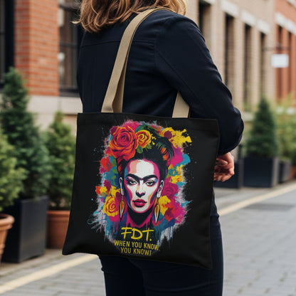 Frida Kahlo portrait on black tote bag with colorful flowers and yellow text.