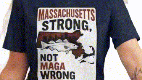 a person wearing a blue t-shirt with a graphic design that includes a fish and the text "Massachusetts Strong, Not MAGA Wrong".