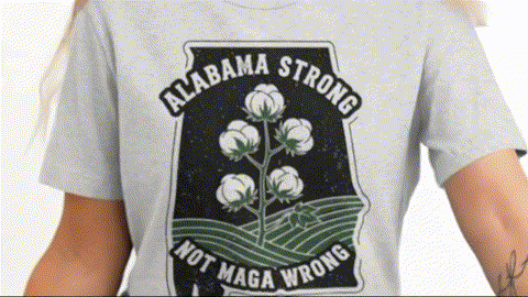 A person wearing a grey t-shirt with a graphic design featuring a cotton plant and the text "ALABAMA STONG NOT MAGA WRONG".