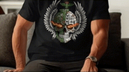 A person wearing a black t-shirt with a skull design and a winged emblem is sitting on a couch.