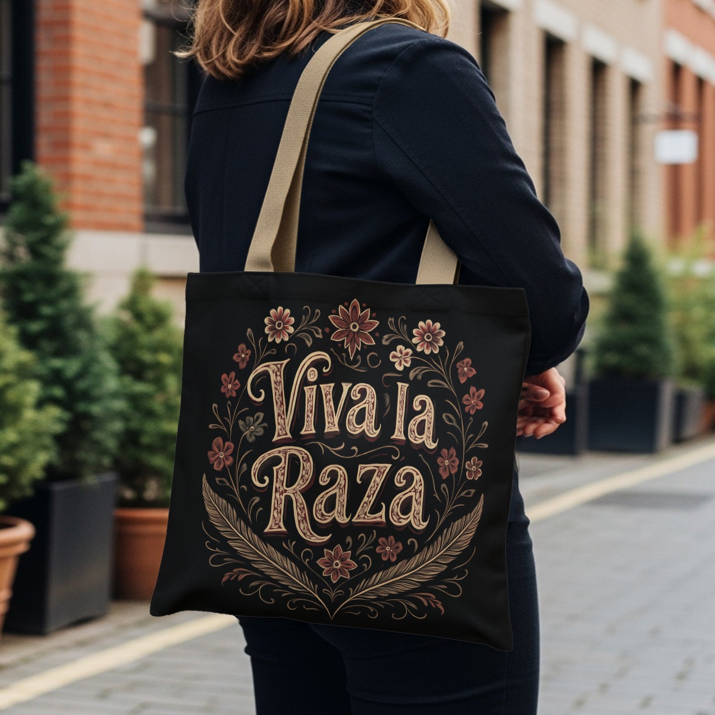 Black tote bag with "Viva la Raza" text and floral border.