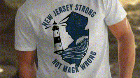 A white t-shirt with a graphic design featuring a lighthouse and a wave, along with the text "NEW JERSEY STRONG NOT MAGA WRONG".