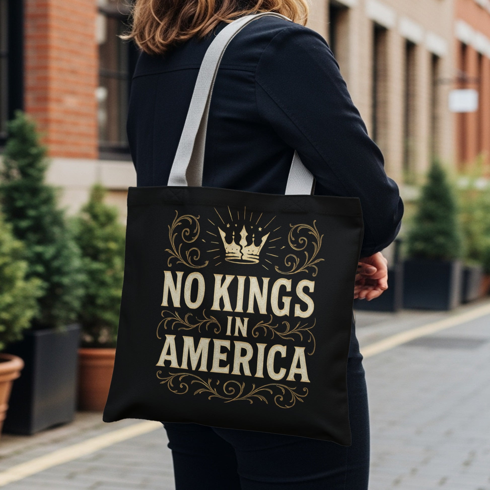 Black tote bag with gold text "NO KINGS IN AMERICA" and crown graphic.