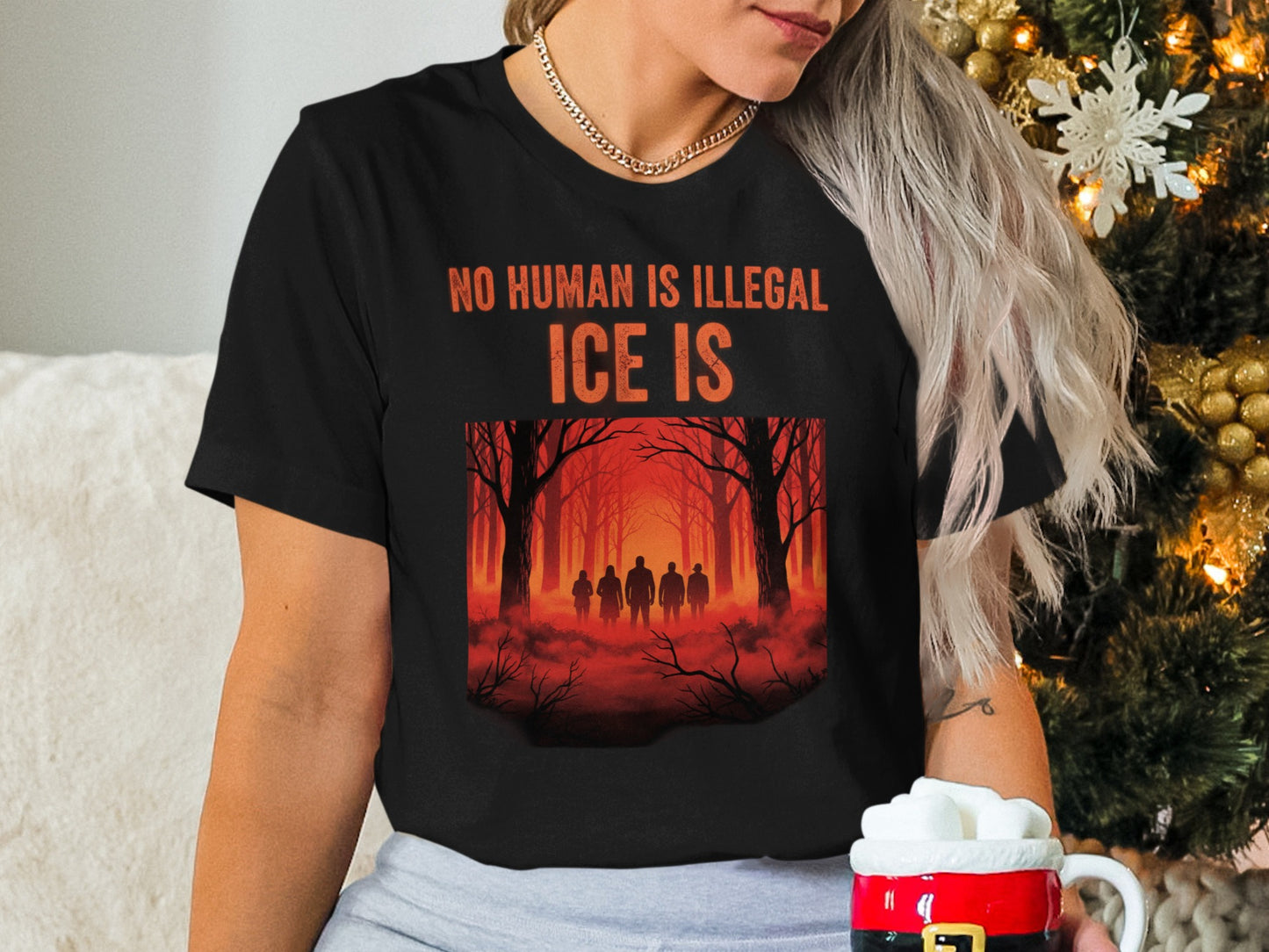 Black t-shirt with "NO HUMAN IS ILLEGAL ICE IS" text and silhouette of people in forest.