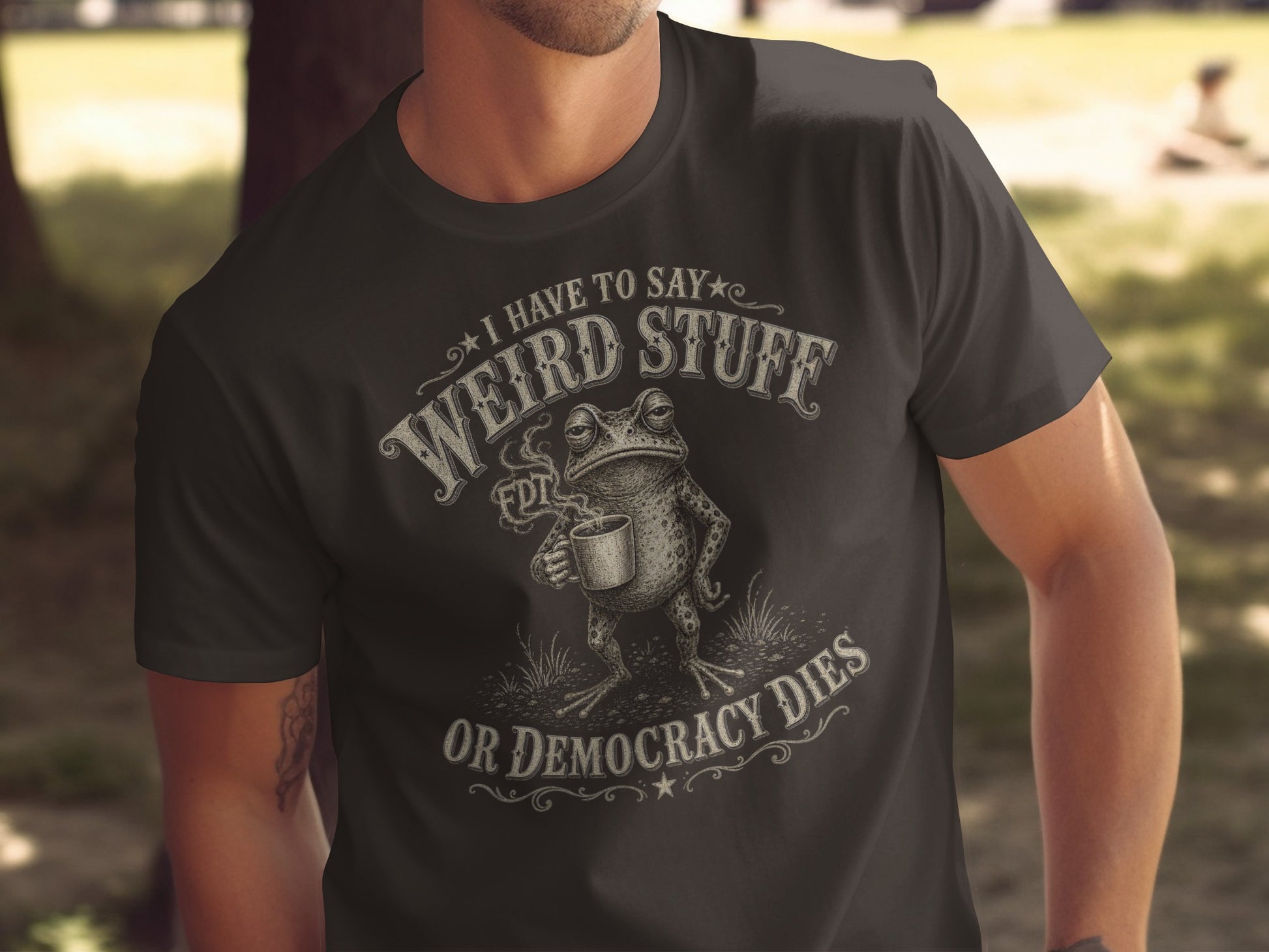 Dark t-shirt with "I have to say weird stuff or democracy dies" text and frog graphic.