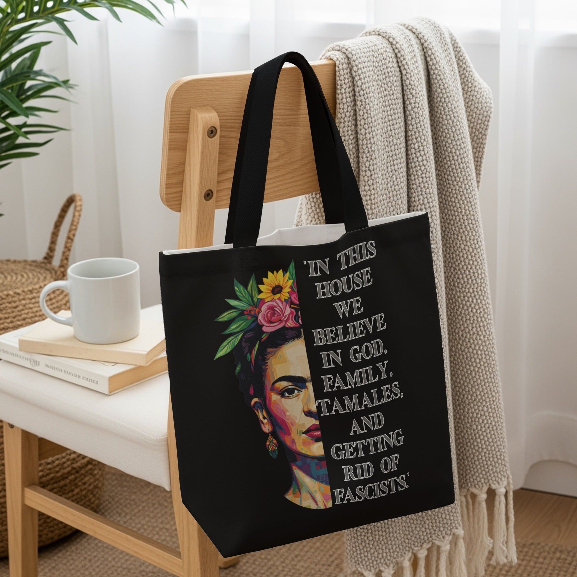 Black tote bag with Frida Kahlo portrait and text "In this house we believe in God, family, tamales, and getting rid of fascists."