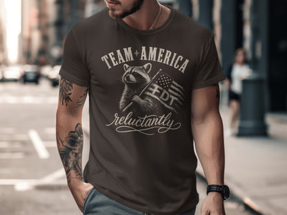 T-shirt with raccoon holding American flag and text "TEAM AMERICA reluctantly".