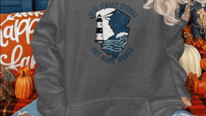 A person wearing a gray sweatshirt with a lighthouse design on it, sitting on a couch surrounded by fall decorations.