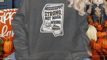 A person wearing a gray sweatshirt with a graphic design on it, standing in front of a display of fall decorations, including pumpkins and a scarecrow.