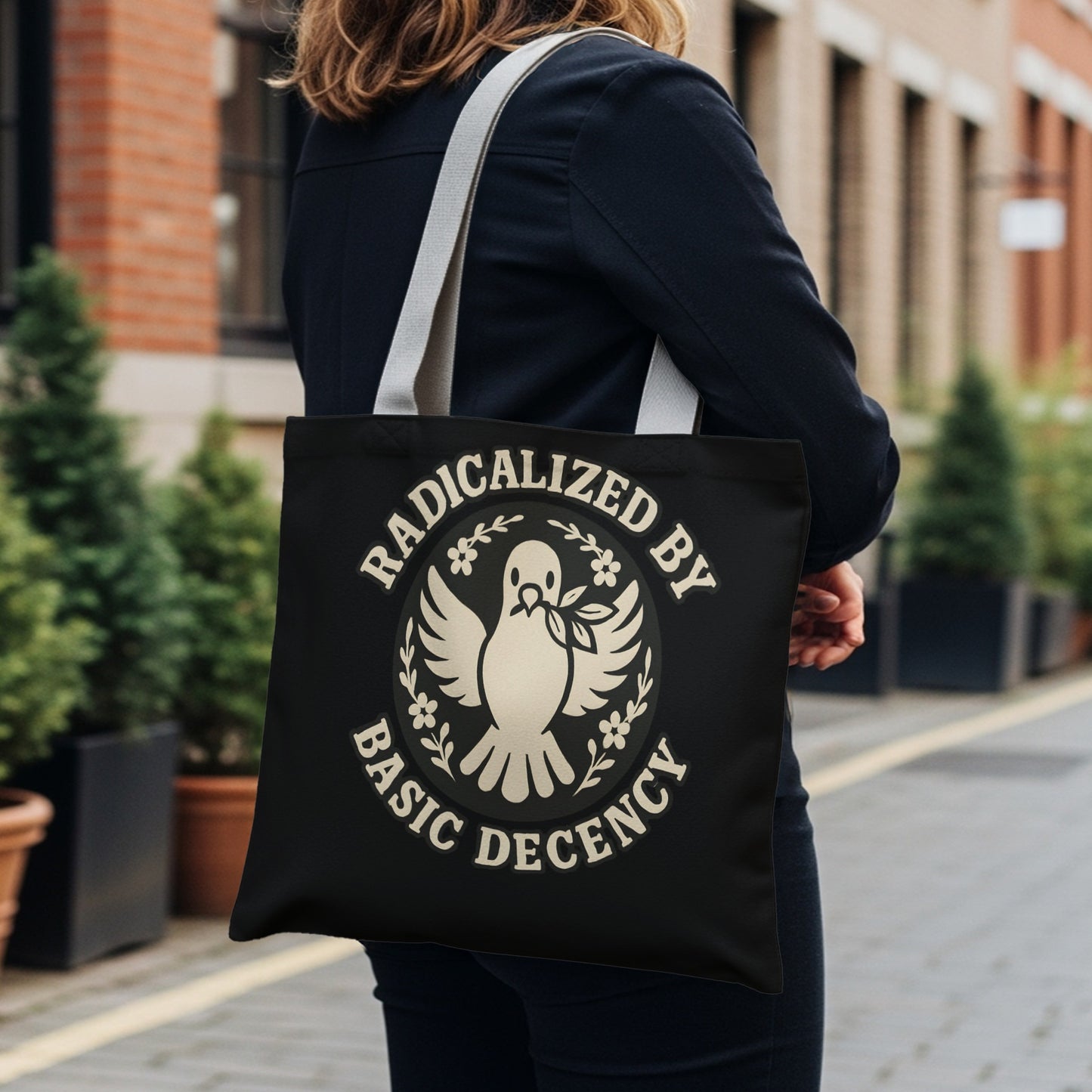 Black tote bag with "Radicalized by Basic Decency" text and dove emblem.