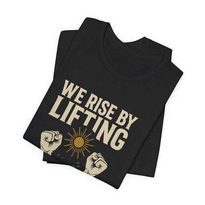 Black t-shirt with "We Rise By Lifting" text and sun/fist graphics.