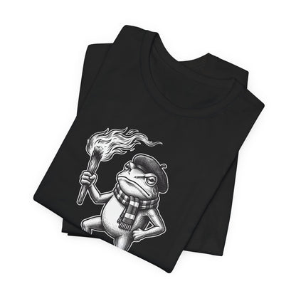Black t-shirt featuring a cartoon frog wearing a beret and scarf holding a torch.