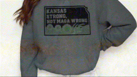 A person wearing a grey sweatshirt with a black and white graphic that says "KANSAS STRONG NOT MAGA WRONG".