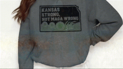A person wearing a grey sweatshirt with a black and white graphic that says "KANSAS STRONG NOT MAGA WRONG".