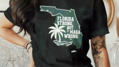 A person wearing a black t-shirt with a graphic design that says "Florida Strong Not MAGA Wrong" printed on it.