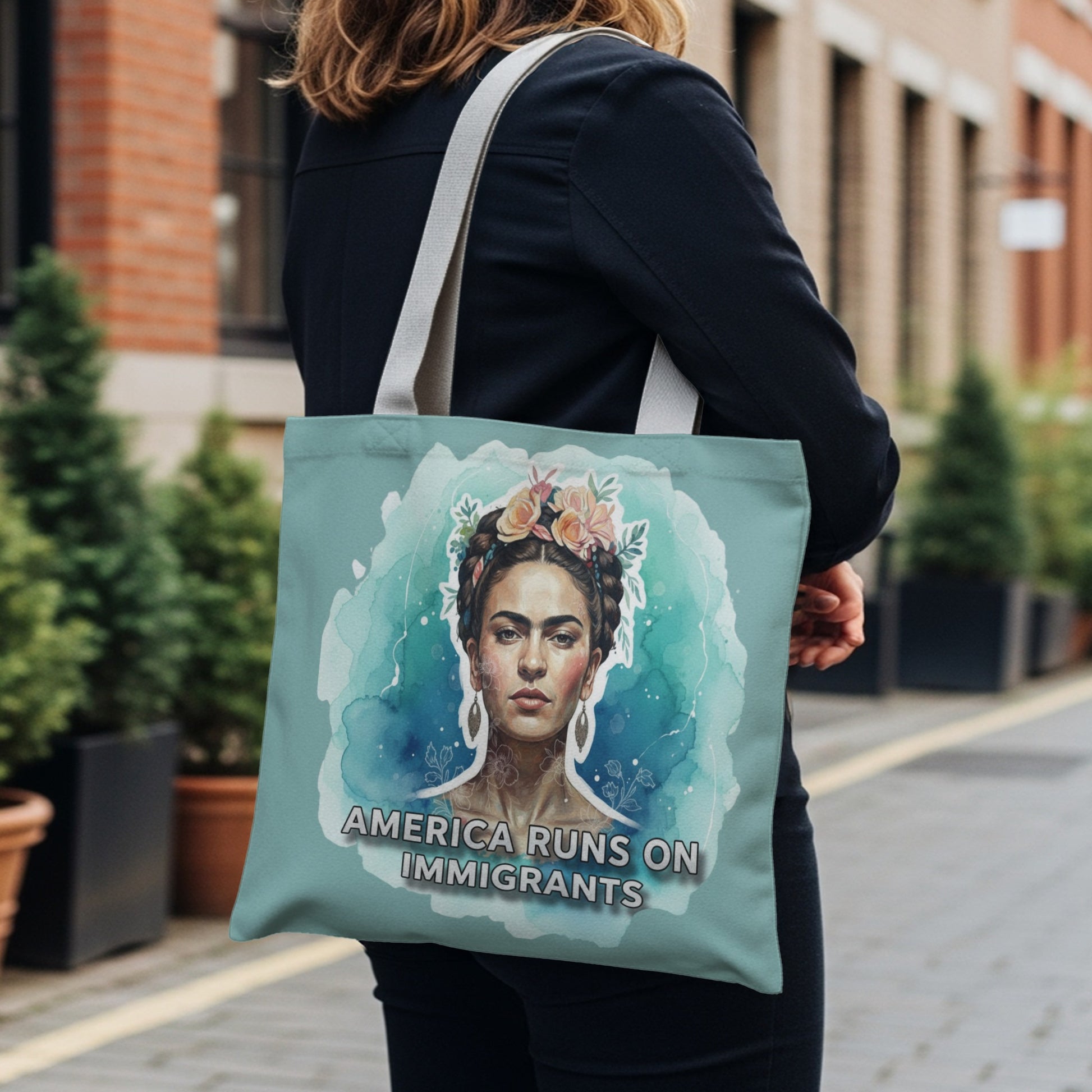 Tote bag featuring a watercolor portrait of Frida Kahlo with flowers, text reads "America Runs On Immigrants".
