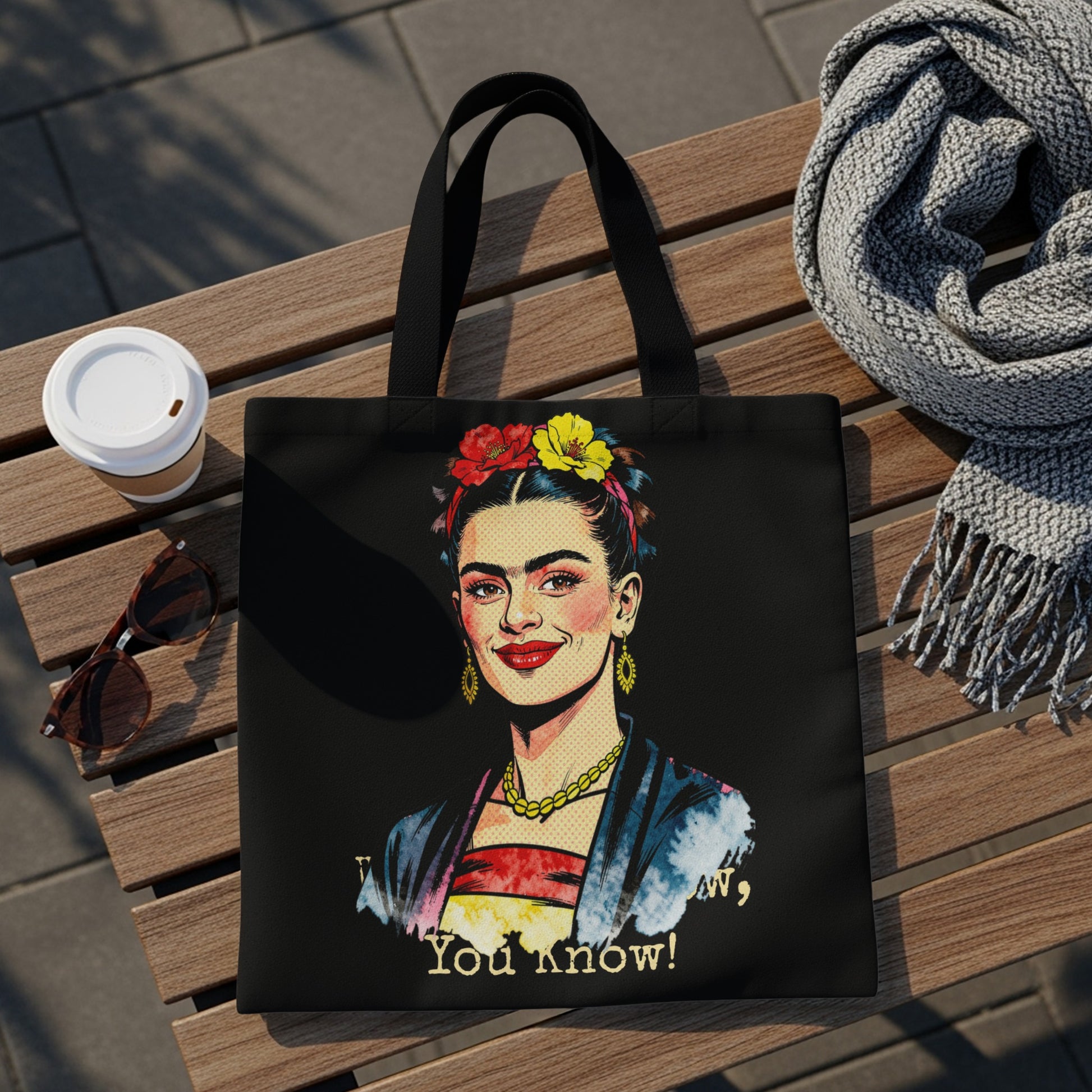 Black tote bag featuring a portrait of Frida Kahlo with colorful flowers and text.