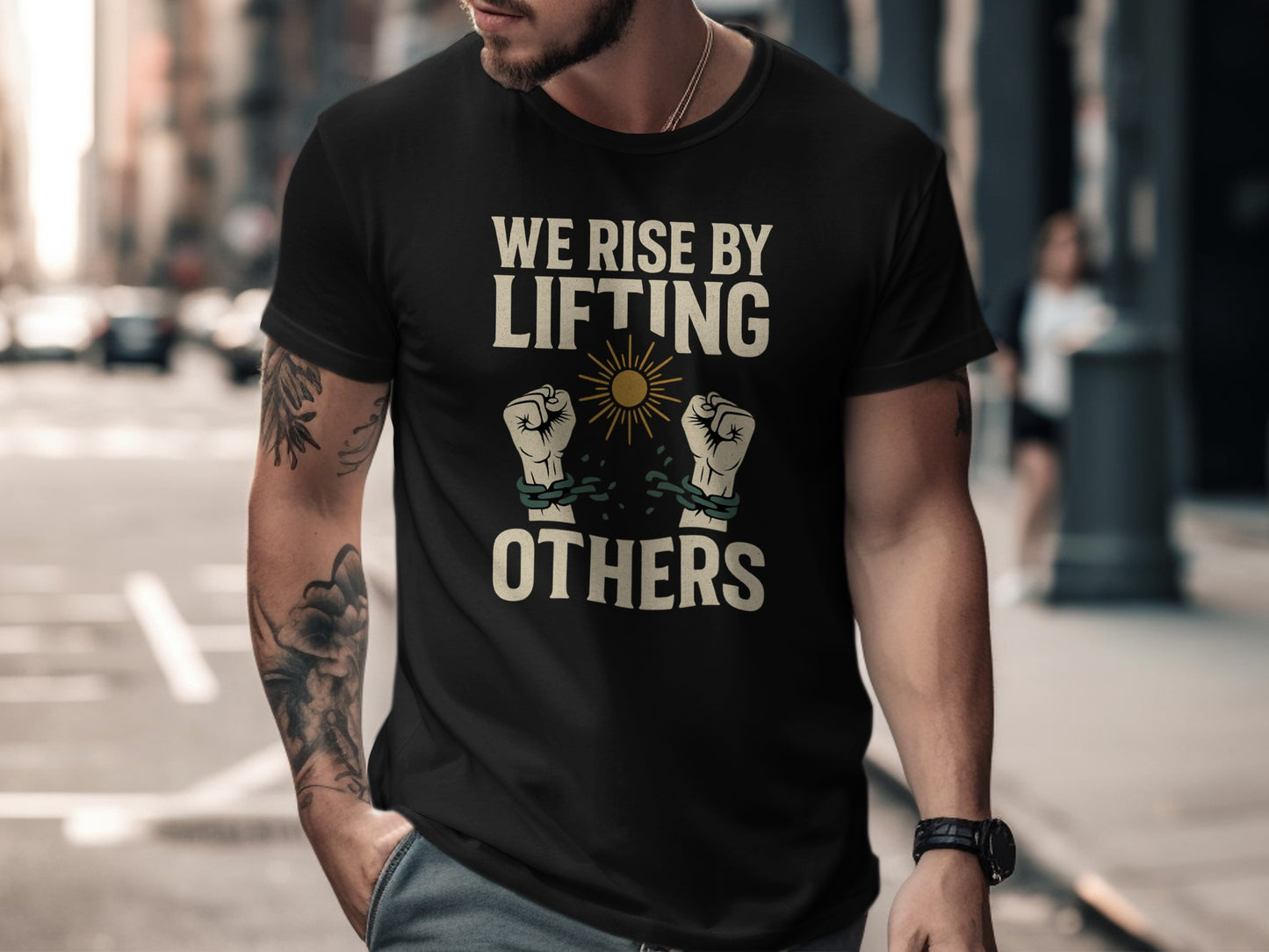Black t-shirt with "We Rise By Lifting Others" text and raised fists breaking chains.