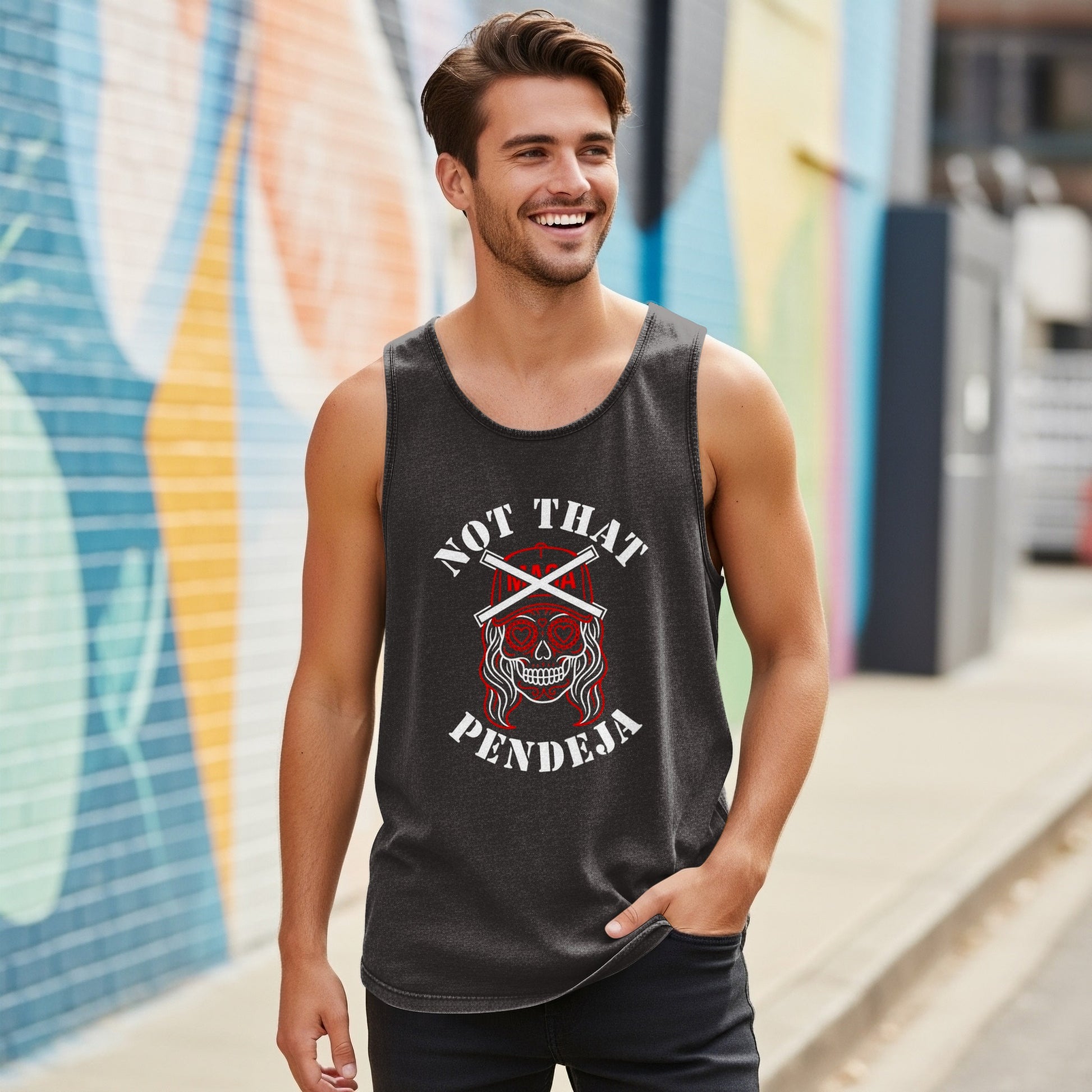Man in charcoal tank top with "NOT THAT PENDEJA" skull graphic, hand in pocket.