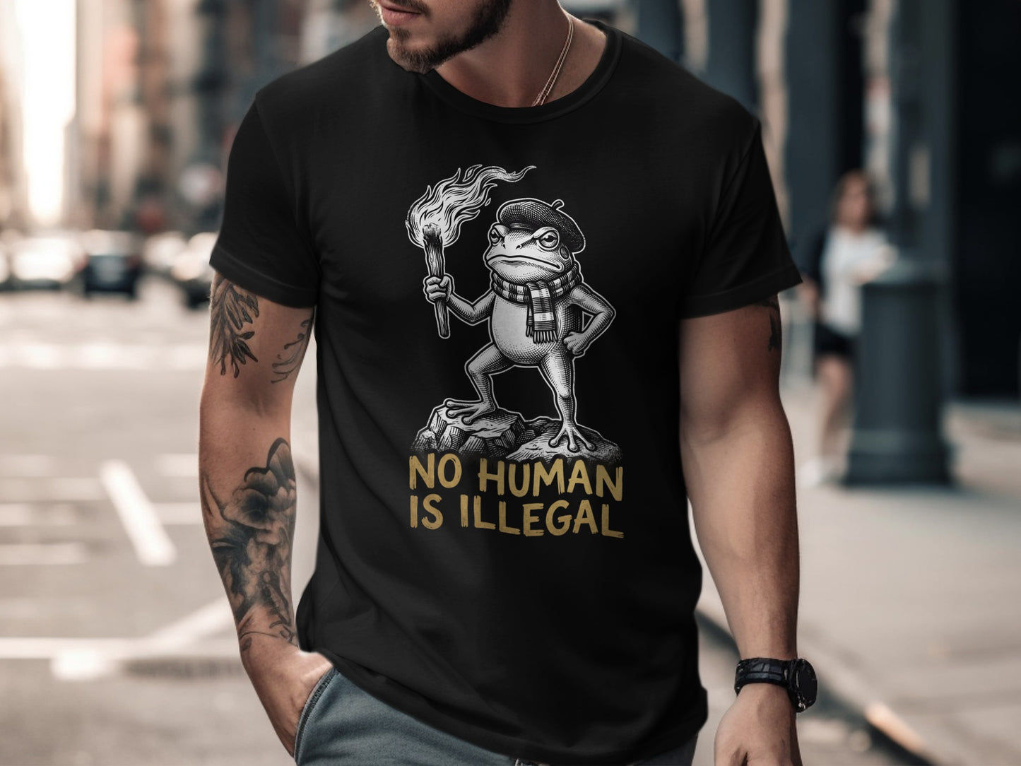 Black t-shirt with a frog holding a torch and the text "NO HUMAN IS ILLEGAL."