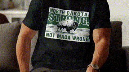 A person wearing a black t-shirt with a graphic design of a buffalo on it, along with the text "NORTH DAKOTA STRONG, NOT MAGA WRONG".