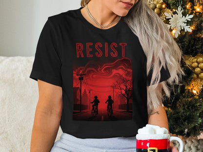 Black t-shirt with "RESIST" text and two people on bikes under a red sky.