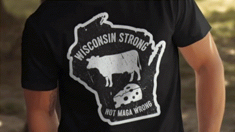 A black t-shirt with a graphic design featuring a cow and a piece of cheese, along with the text "Wisconsin Strong" and "Not Maga Wrong".