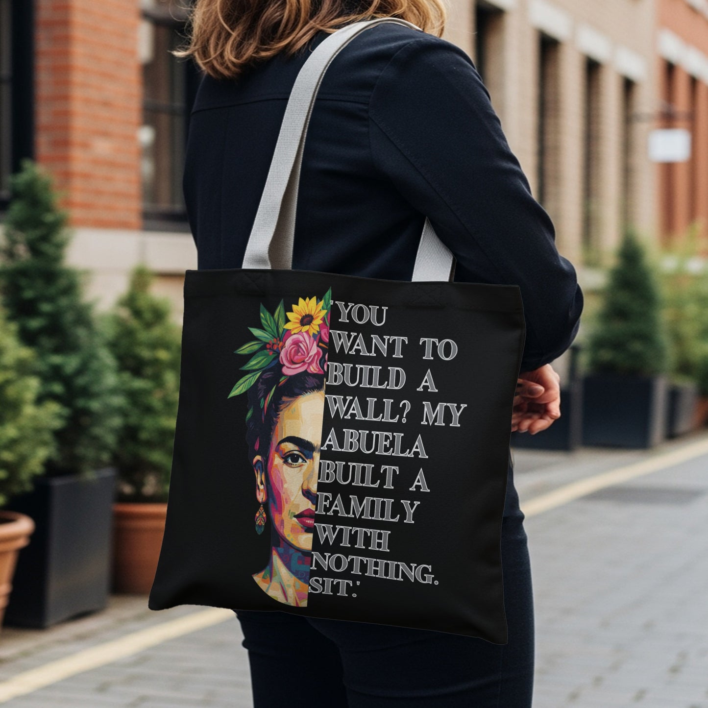 Black tote bag with Frida Kahlo portrait and empowering Spanish text.