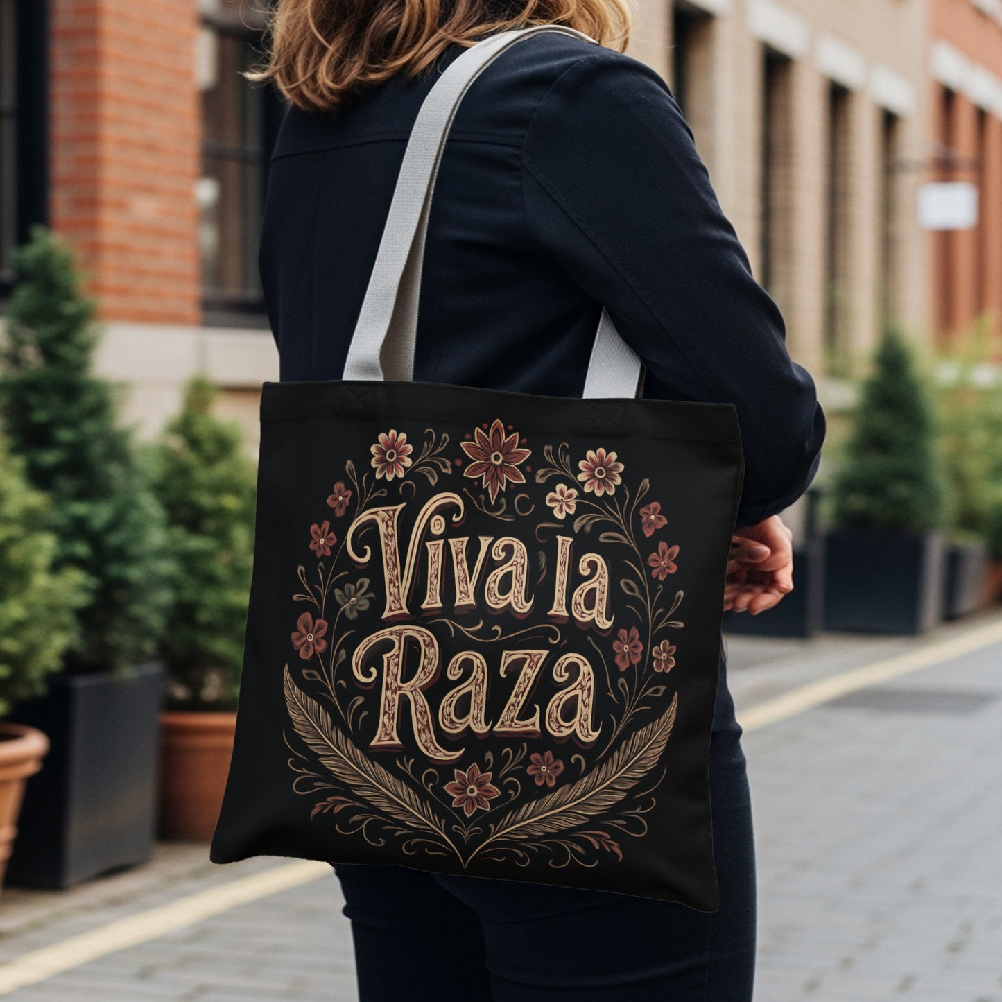 Black tote bag with "Viva la Raza" text surrounded by floral and feather design.
